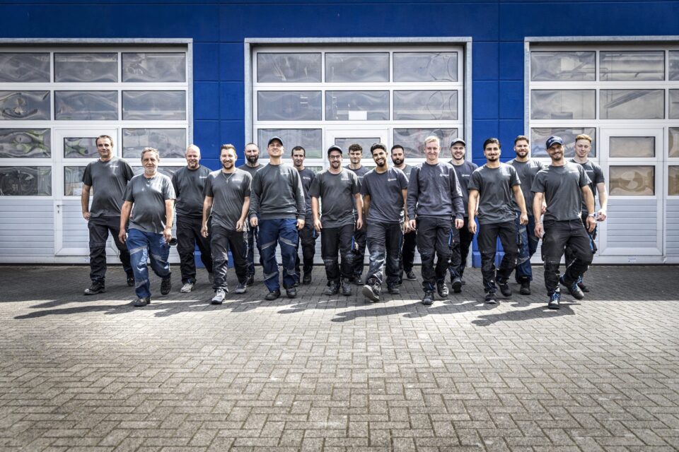 Team vor Werkstattgebäude in Arbeitskleidung