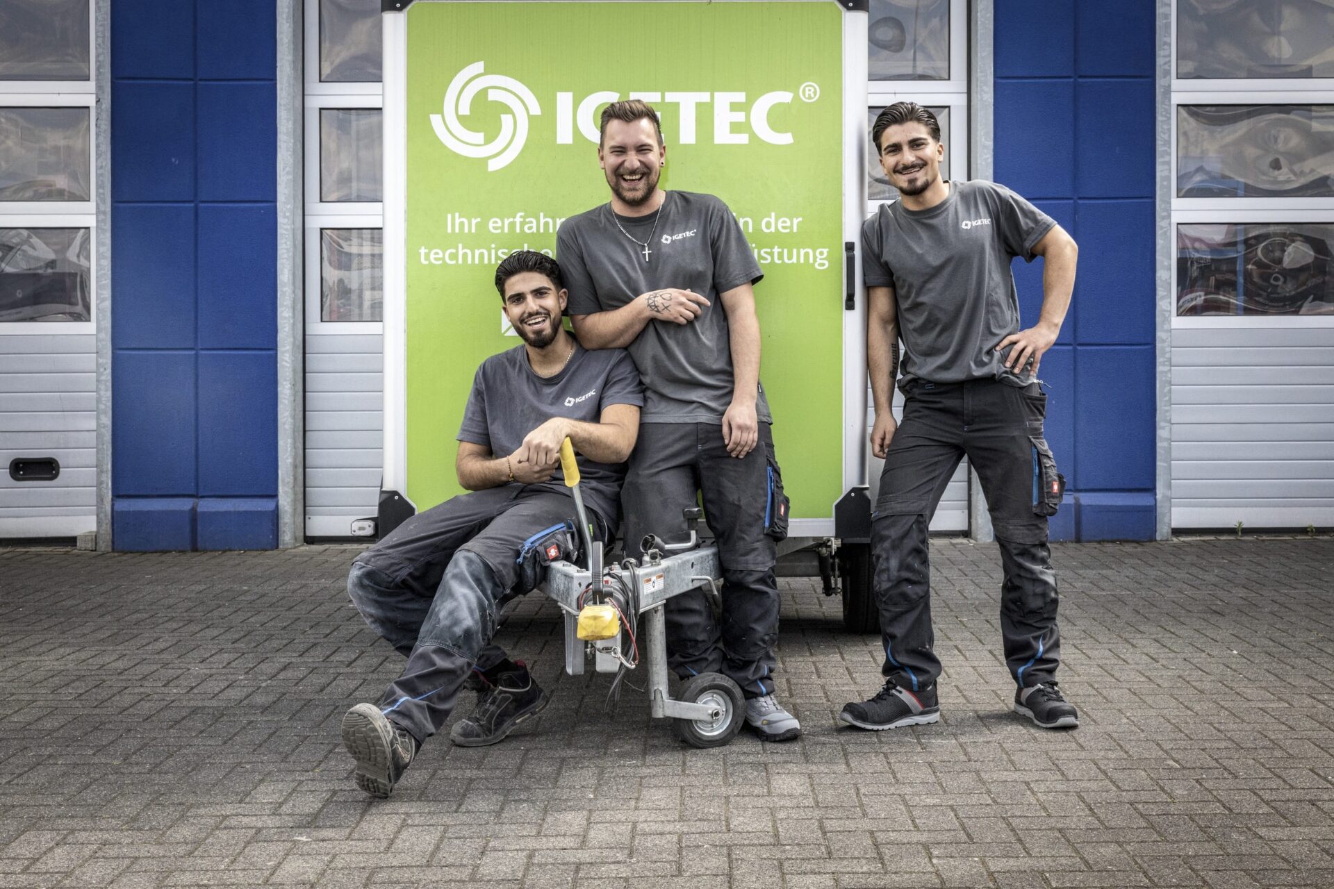 Drei fröhliche Technikarbeiter vor grünem Schild