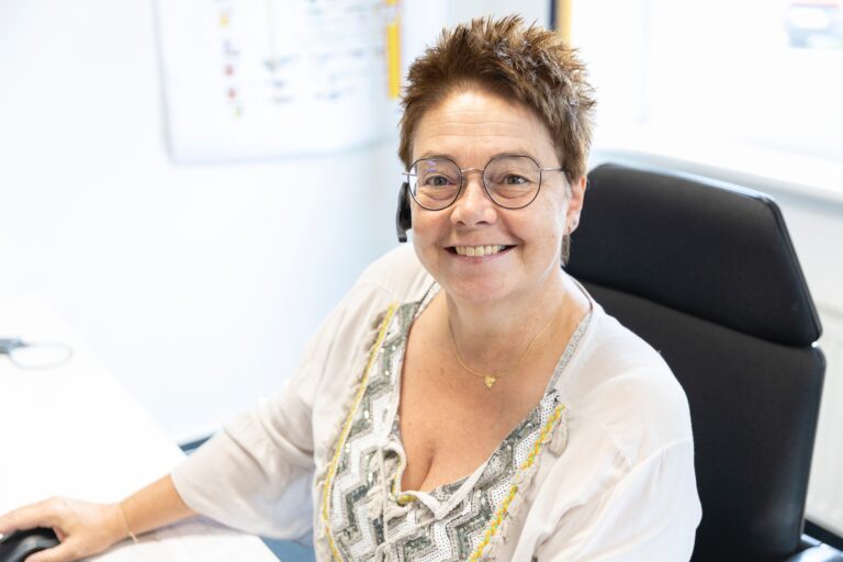 Lächelnde Frau mit Brille im Büro sitzt am Schreibtisch.