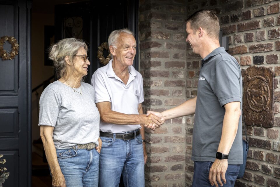 Person begrüßt älteres Paar vor dem Haus
