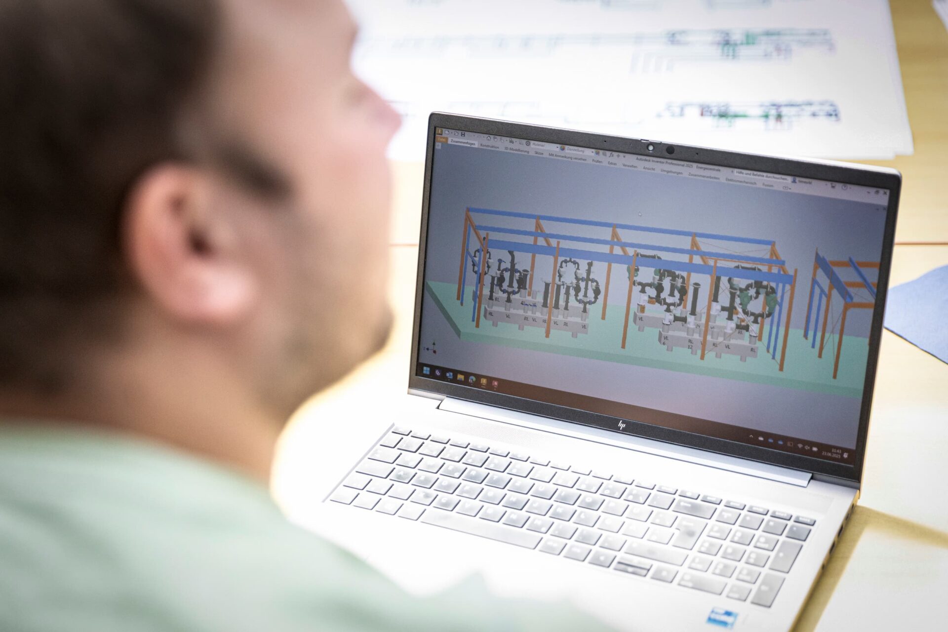 IGETEC-Mitarbeiter betrachtet am Laptop ein 3D-Modell einer technischen Anlage mit Rohrleitungen und Gestellen.