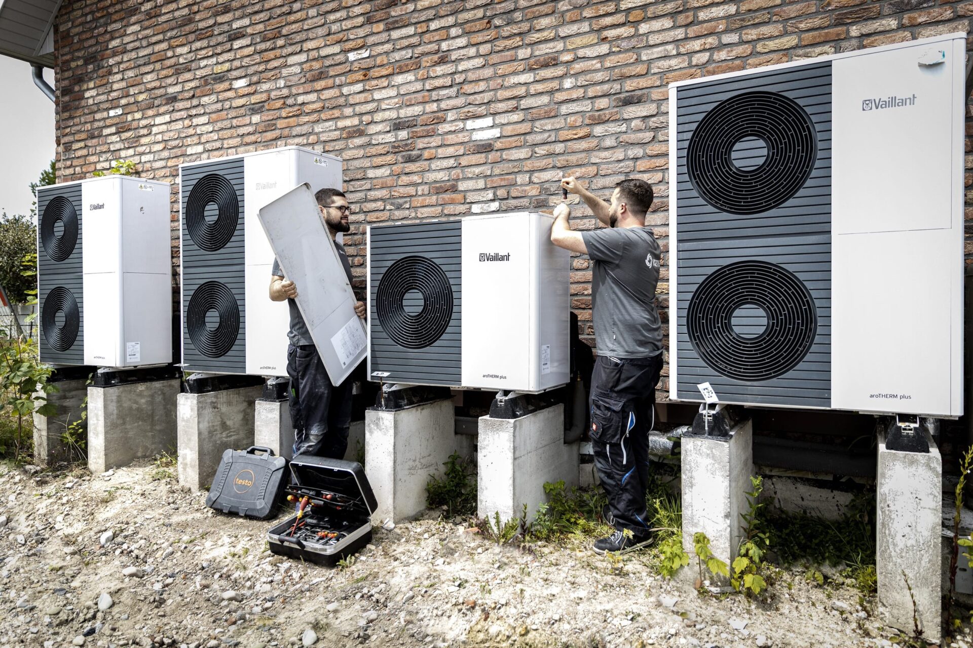 Techniker installieren Wärmepumpen an Backsteinmauer.